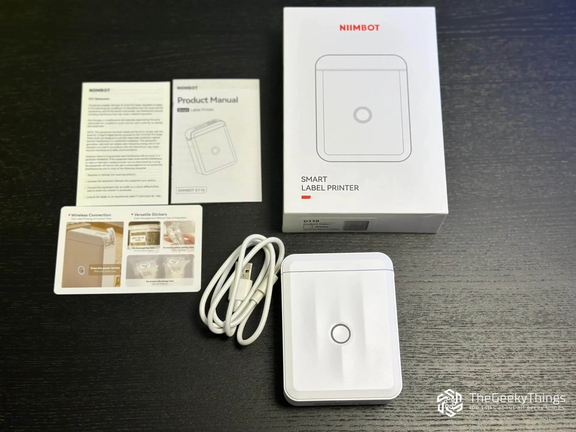 Niimbot D110M with the box, manual, and charging cable on the desk